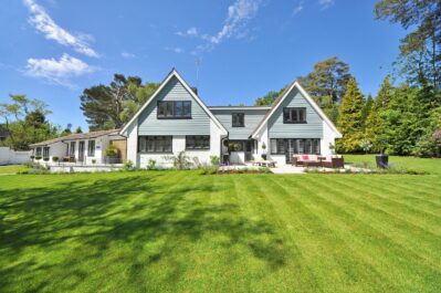Modern family home exterior showcasing a large lawn and garden under a clear blue sky.